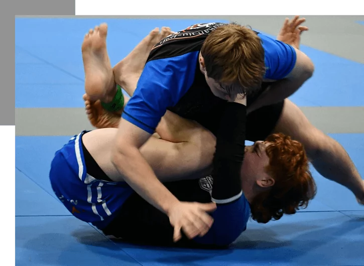 Two martial artists grapple on mats, practising guard position in no‑gi training