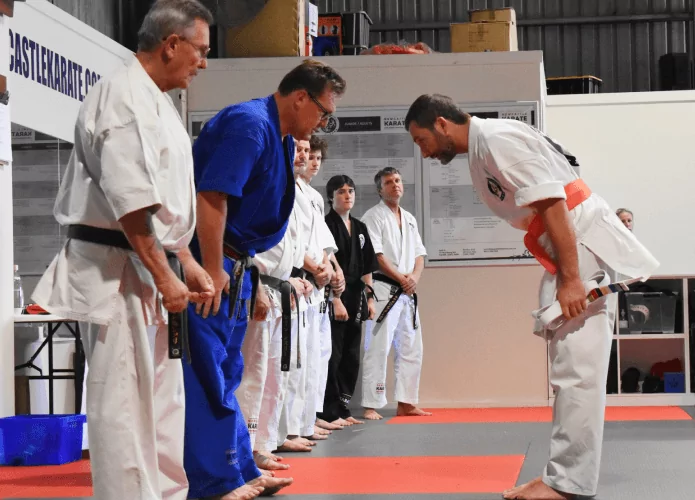 Karate student with orange belt bows respectfully while holding certificate in dojo ceremony