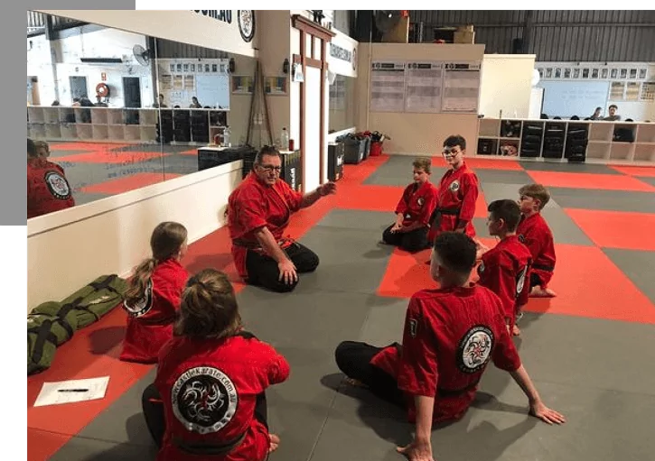 Shihan Marc speaks to young students seated in semicircle during dojo lesson.