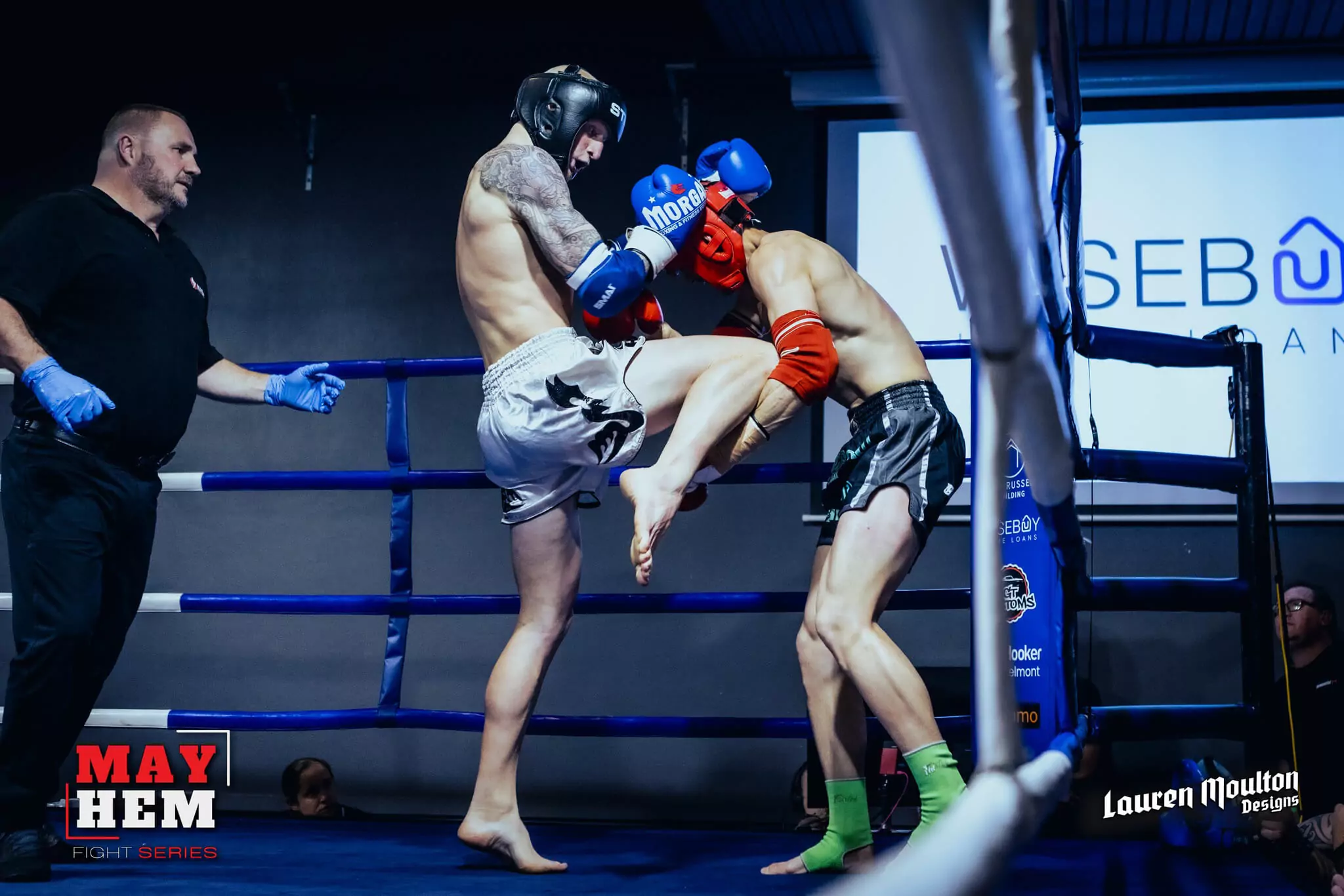 Kickboxing match shows blue-gloved fighter delivering knee strike to red-gloved rival