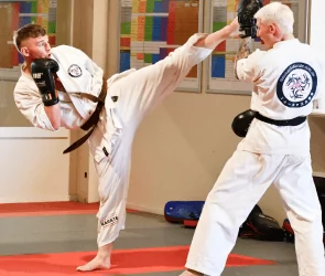 Two black belt karate students spar in dojo, one delivering a high kick while the other blocks