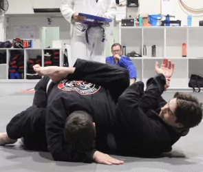 Two Brazilian Jiu‑Jitsu practitioners grapple in guard position while instructor observes