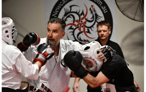 Karate instructor guides two adult students sparring with protective gear in dojo