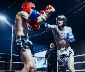 Two fighters in headgear spar in boxing ring as referee watches closely