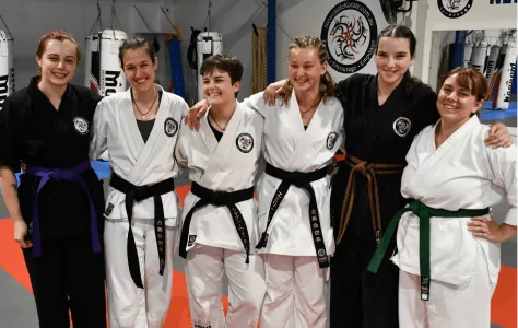 Group of martial artists in belts pose together in dojo after training session